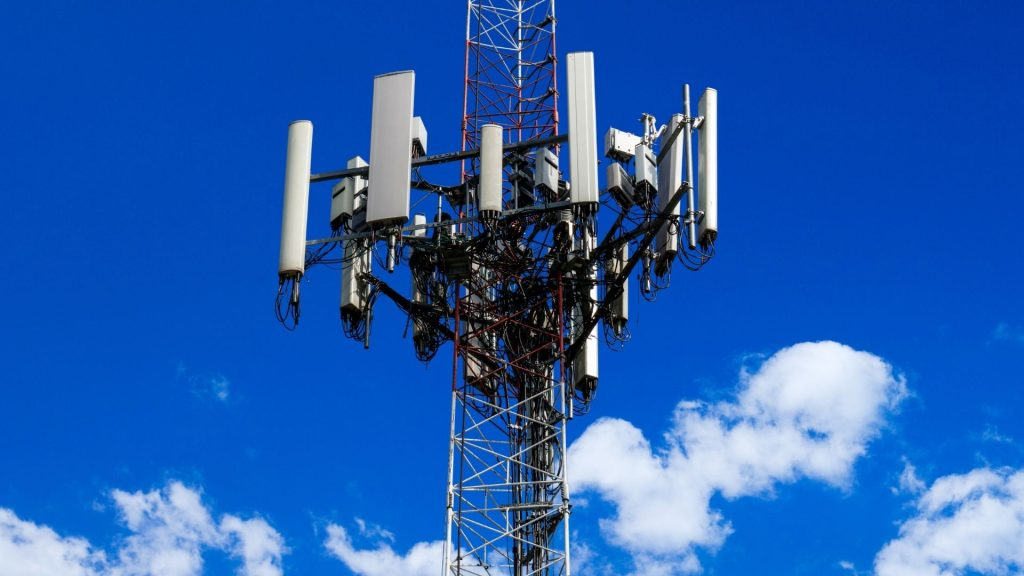 Full view of a cell tower with antenna equipment against a bright blue sky